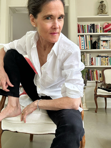 Ann at home in black denim and an easy-fitting button down made of crisp white poplin. You can just make out George Mashburn (a tabby cat) asleep on a chair beneath their bookshelf.