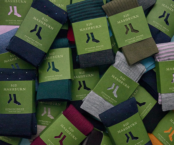 close-up of a big pile of our sock assortment, there's olive, navy, deep red, a bright orange, a pale gray, lavender — all packaged in SM green paper