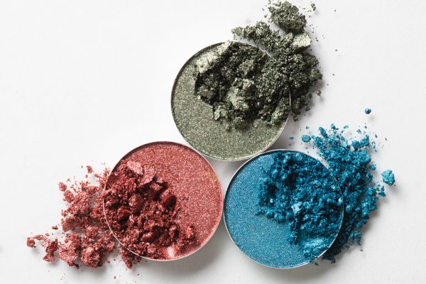 A dynamic photo of three different containers of mica powder eyeshadow, with bits of the eyeshadow spilling out of them.