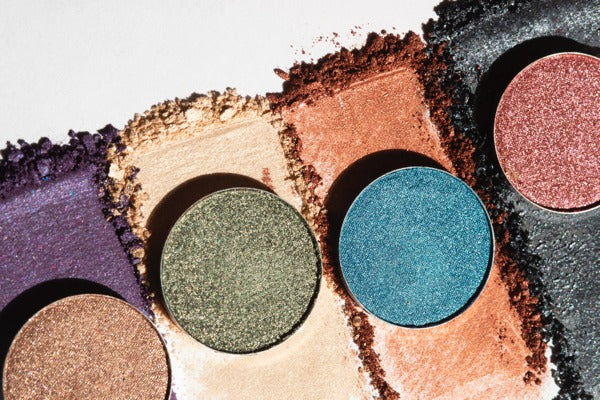 Several eyeshadows spread on a white surface, with additional eyeshadows in containers resting on top of the different spreads.