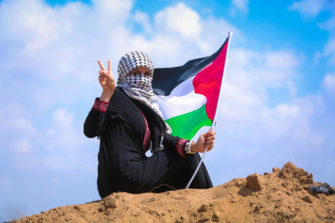 Palestine gaza woman wearing black and white keffiyeh around head and holding palestine flag