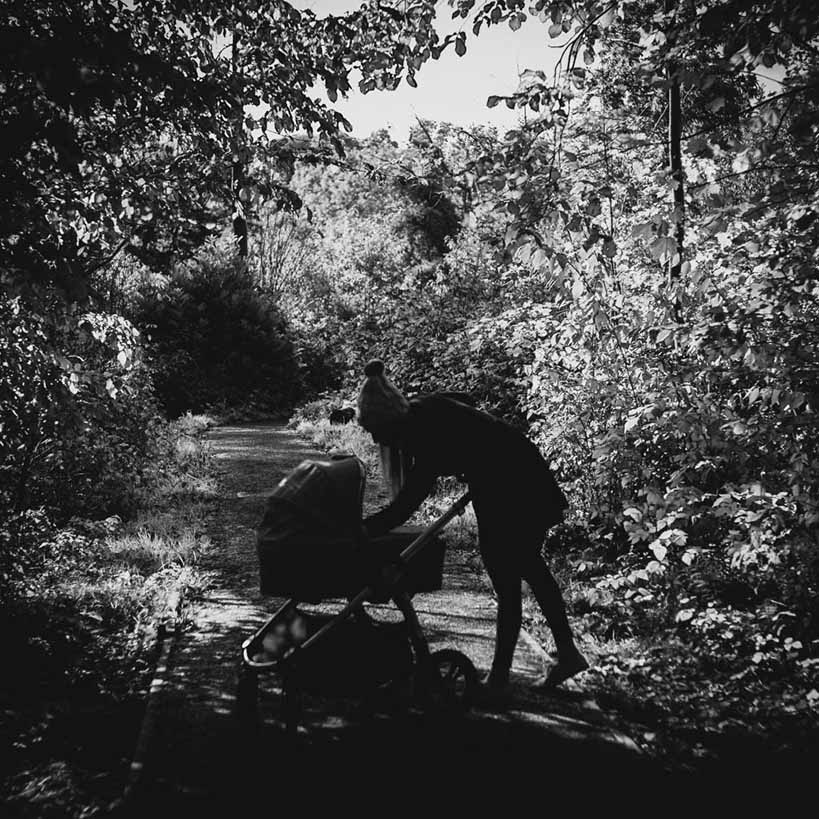 A black and white image of Katerina and her Ocarro Moon pushchair in a wooded area.