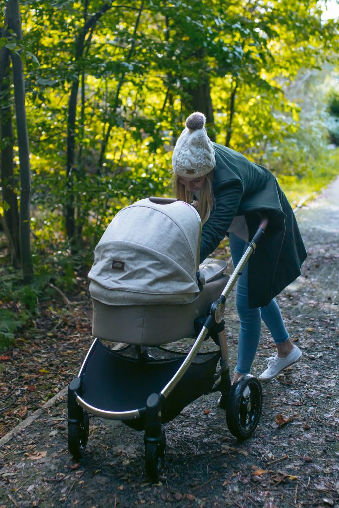 Katerina is attending to her baby while it is in the Ocarro Moon pushchair carrycot, they are walking through the woods.