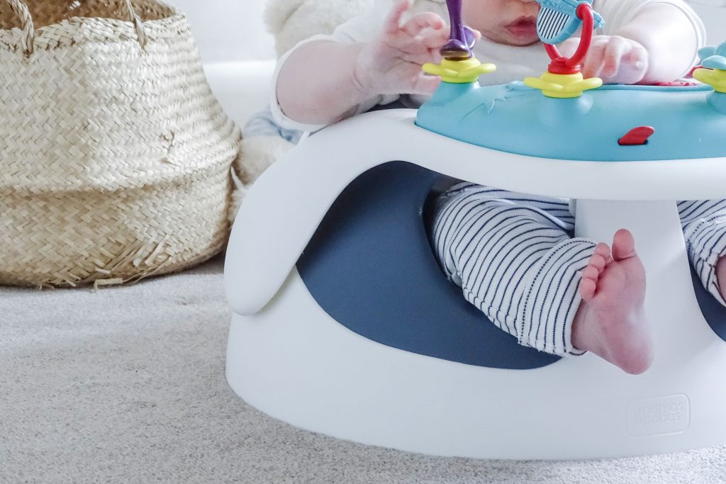 A close up of the Baby Snug booster seats wide base. Baby Marlow is sat in it, playing with the toy tray.