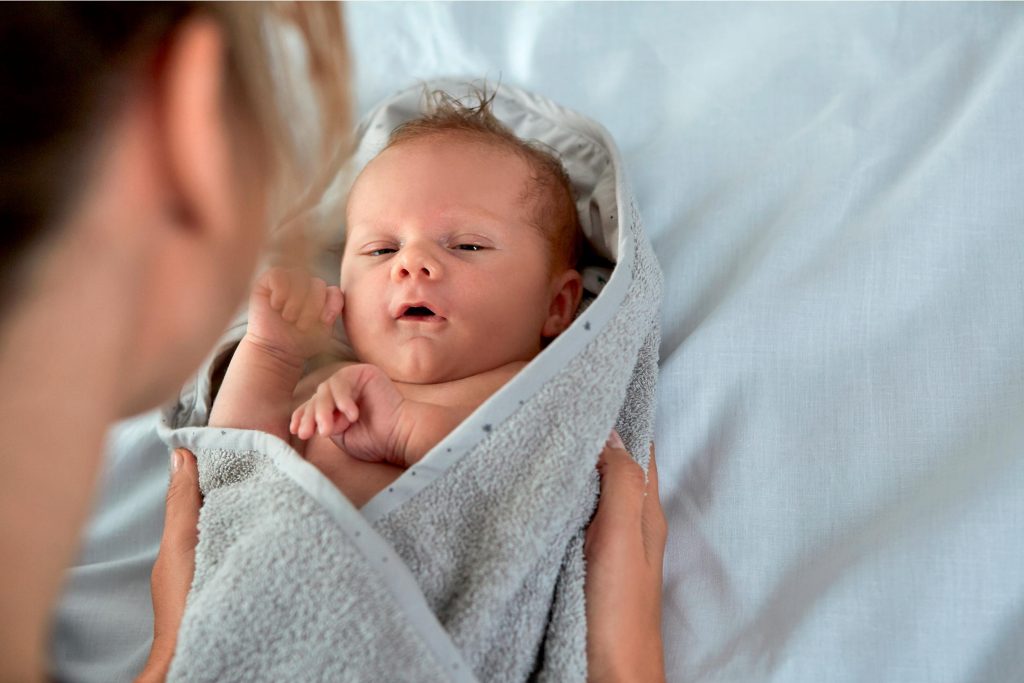 A mother is swaddling her newborn baby in a towel and is cooing at it while the baby watches her.