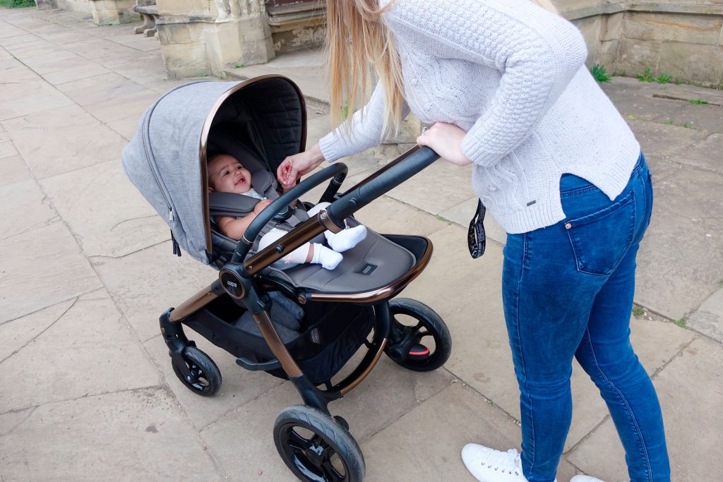 Haley is pushing baby Elodie in the Ocarro pushchair along a pavement, she is reaching inside the pushchair to settle the baby.