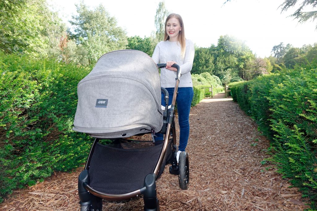 Haley is pushing the Ocarro pushchair along a gravel path between two rows of hedges.