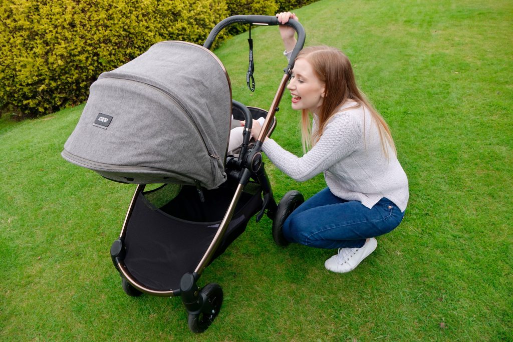 Haley is crouched next to the Ocarro pushchair, talking to baby Elodie. She is in a park, on the grass.