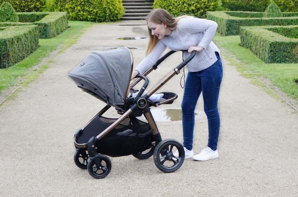 Haley is pushing baby Elodie in the Ocarro pushchair along a gravel path. She is leaning in to the pushchair to reassure the baby.