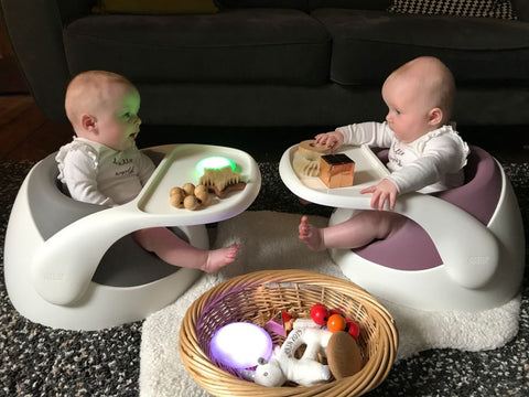 The twin babies, Esther and Eve, are sat in their Baby Snug booster seats and have been positioned to face each other. 