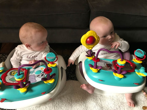 Twin babies, Esther and Eve, are sat in their Baby Snug Booster seats with the activity trays attached, they are playing and interacting with the brightly coloured toys.