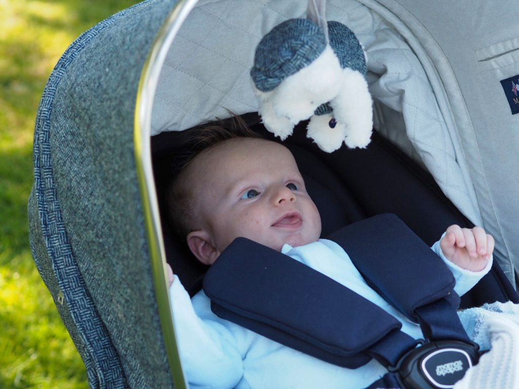 Image of baby Freddie sat in the Ocarro pushchair, wide awake looking at a soft toy that's hanging down from the pushchair hood.