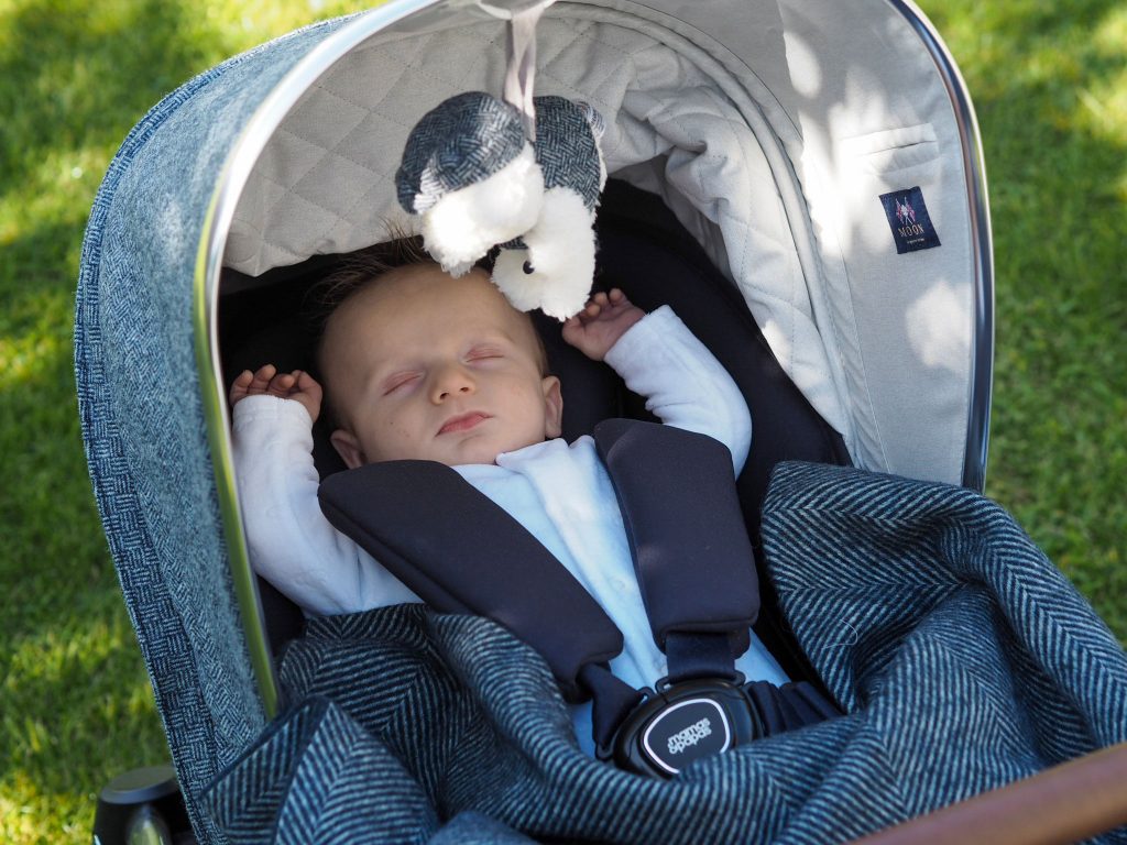 Image of baby Freddie in the Ocarro Moon pushchair asleep. The pushchair hood is pulled up and a soft toy hangs down above him.
