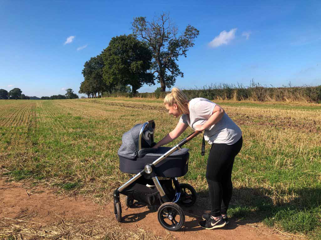 Image of Harley pushing the Ocarro Moon pushchair along a dirt track in the middle of a field.