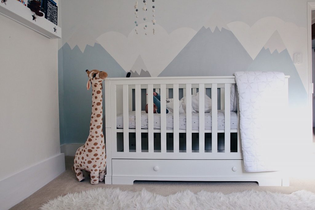 Image of the cot bed in a nursery, with a giraffe soft toy.