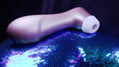 Sitting on a blue and purple shiny sequined background is a bronze coloured long object which has a white rubber round ring at one end that has a small opening.