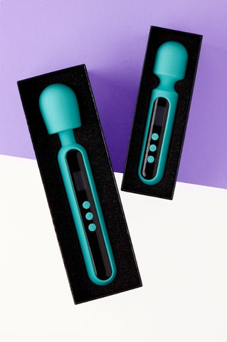Two teal green rubber wand shaped objects lay flat and are encased in a black border. One is slightly larger than the other and the background is half white and half purple.