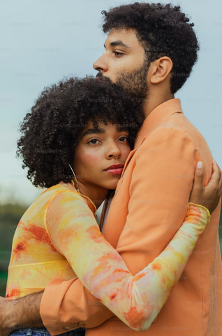 A couple are pictured both wearing orange and facing each other. The woman has her head pressed against the man's chest in an embrace.