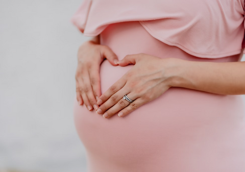 On a white background a woman' large pregnant stomach is pictured at close range and she is wearing a tight pale pink shirt.