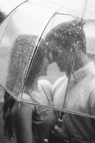 A couple are pictured in close range under the same umbrella staring into each other's eyes and smiling.