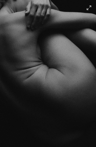 A black and white image of a naked woman curled up in a ball with only her side visible.