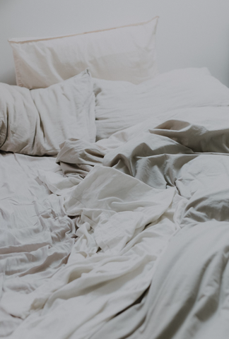 A zoomed in picture of an unmade bed with just white sheets all messy looking pictured.