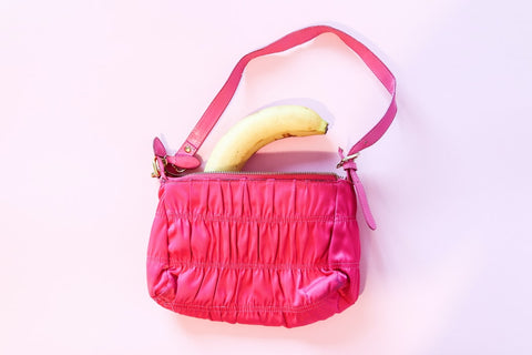 On a pale pink background a pink leather handbag is pictured with a banana poking out from inside the bag.