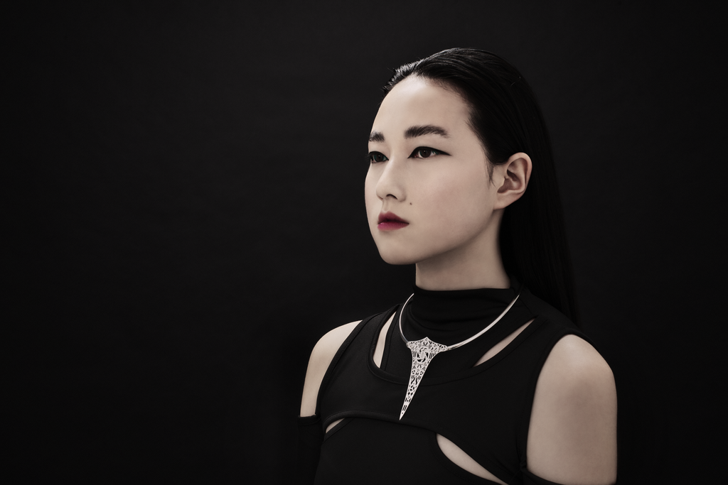 An asian model wearing a graphic cut out black dress paired with a stunningly detailed goth choker in rigid metal con delicate gothic inspired filigree. Positioned on a full black background gives the idea of refined dark luxury