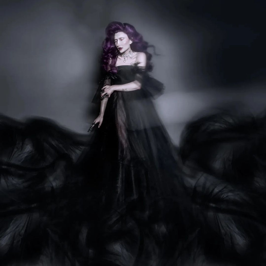 A high fashion shoot featuring a model with long purple hair. The model wears a long and wide black gown paired with an intricate studded choker in goth style. The overall style exudes a dark and mysterious aesthetic.