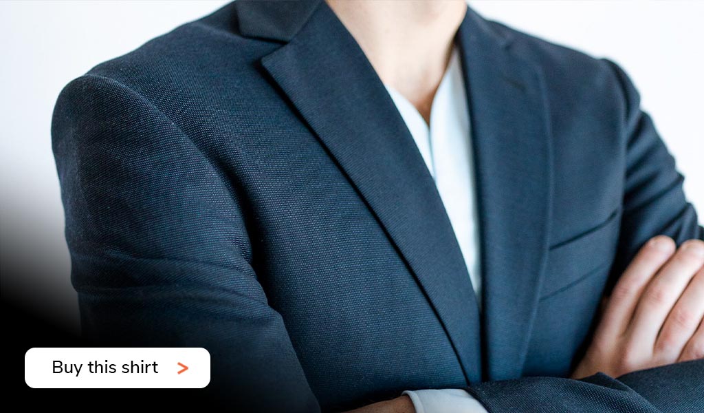 A close up of a man crossing his arms wearing a Cheegs collarless dress shirt in light blue with a suit jacket.