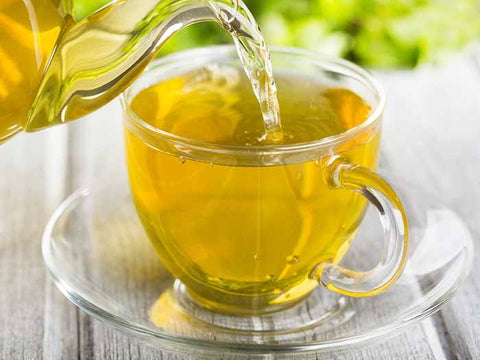 yellow tea being poured into a clear tea cup