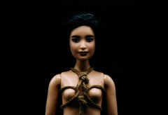 a black background with a barbie tied up in a rope chest harness