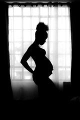 a silhouette image of a pregnant person in front of a window with their hand gently on their bump