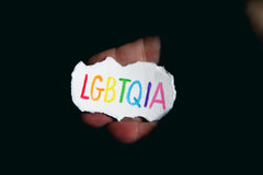 a black background with a small piece of ripped white paper with rainbow lettering spelling LGBTQIA
