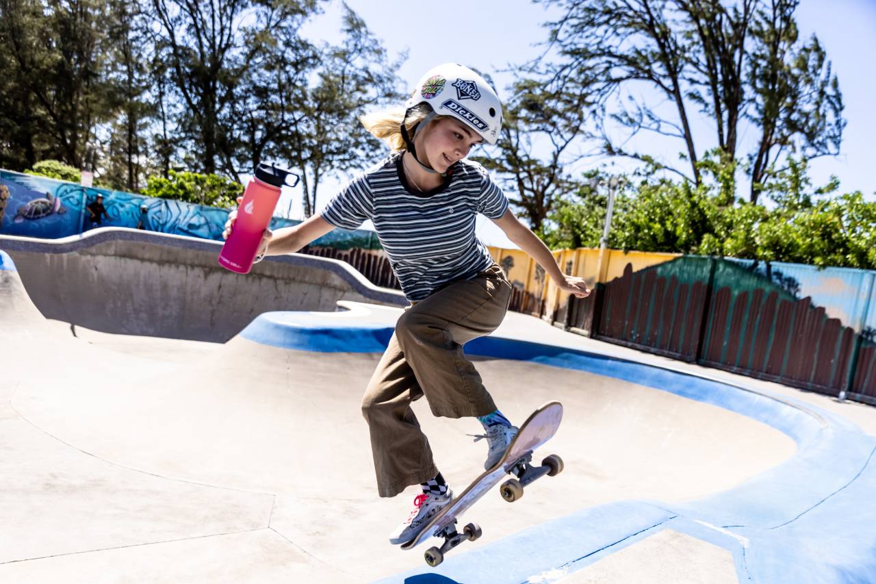 A young girl holding a water bottle while skateboarding