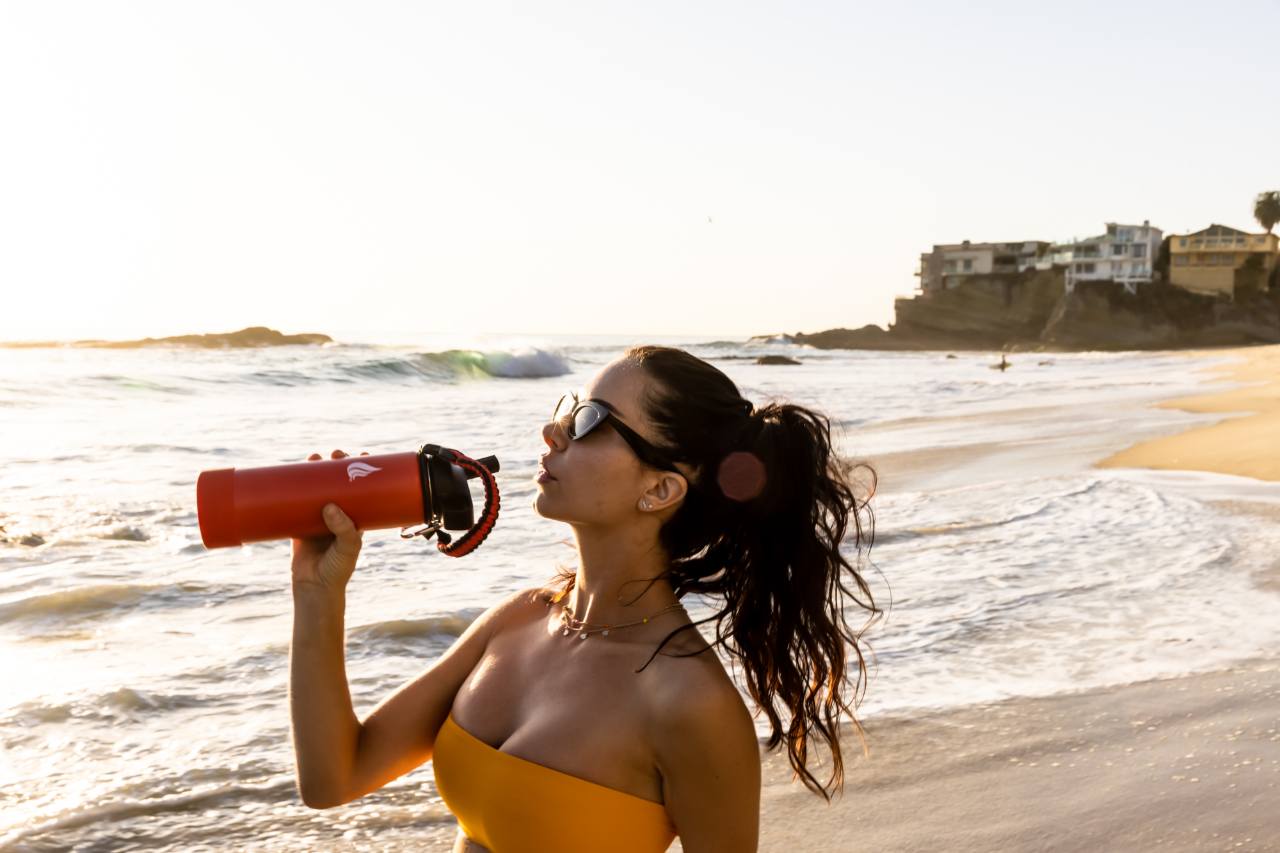 A woman in an orange swimwear drinking from a stainless steel water bottle