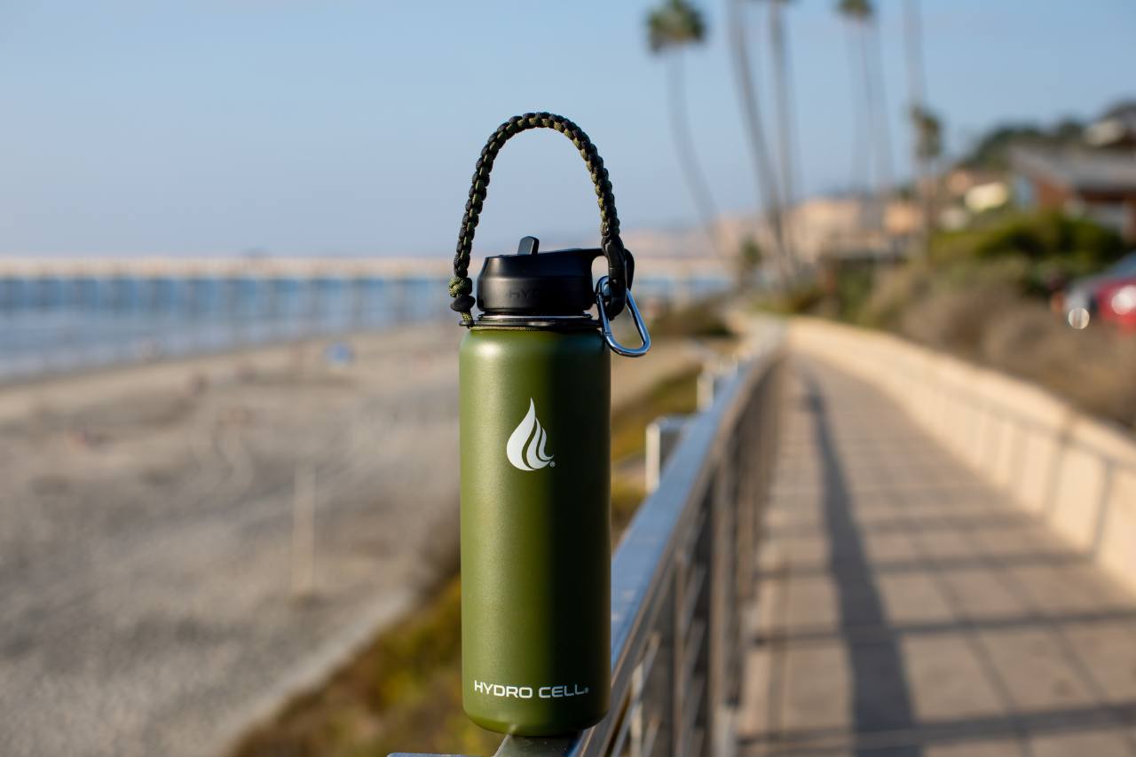 A stainless steel water bottle placed on a railing near the beach