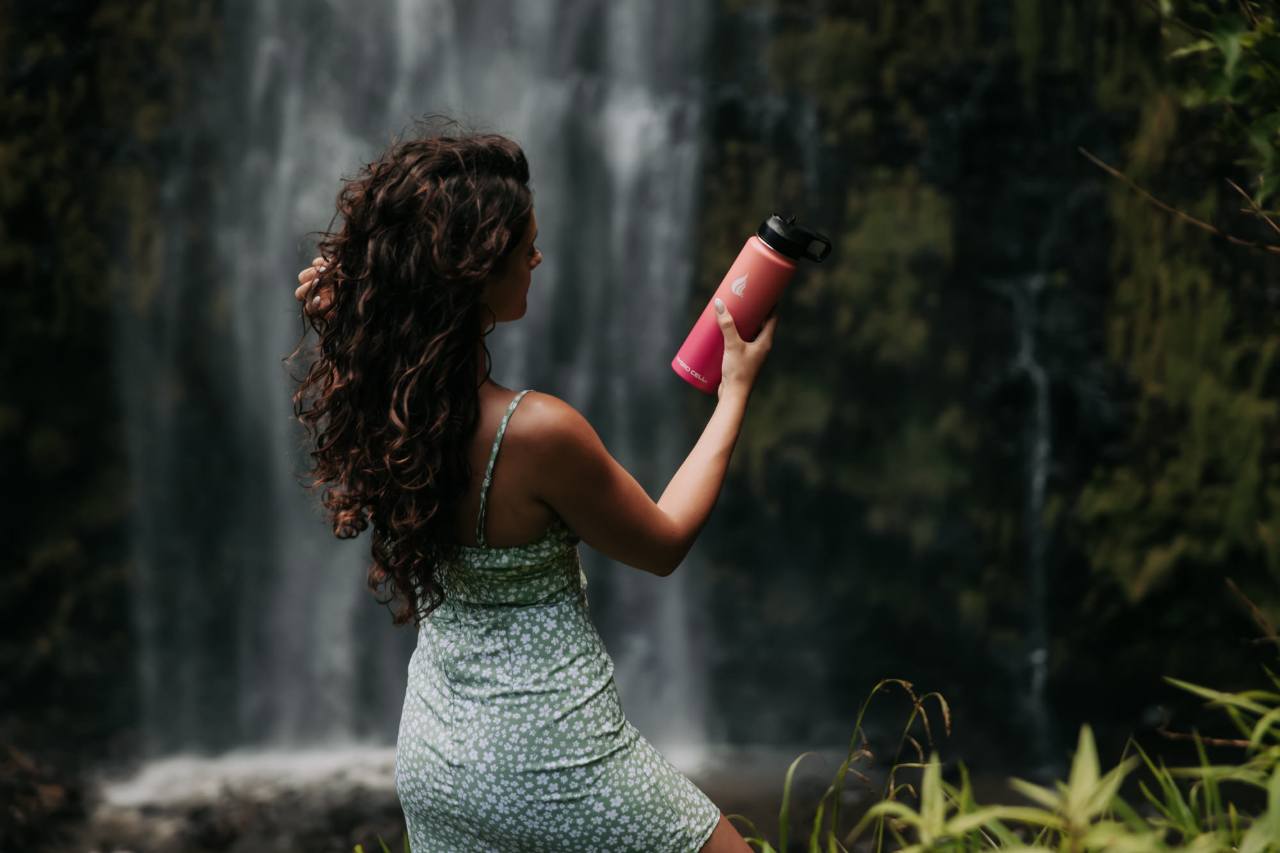 A woman standing near waterfalls holding a pink water bottle