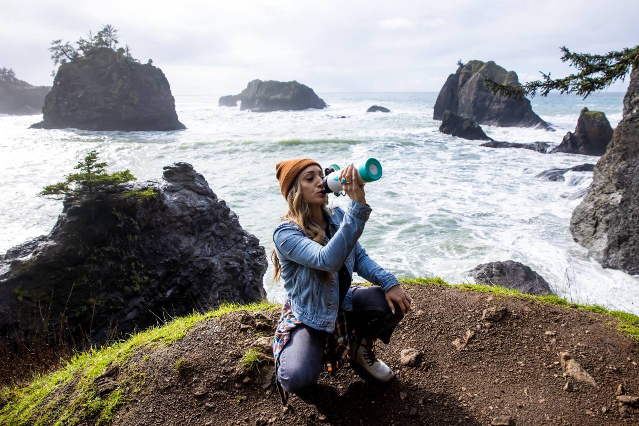 A woman sitting at the edge of a cliff while drinking from a water bottle