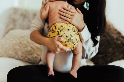 A mother holding her baby who is wearing a yellow cloth nappy