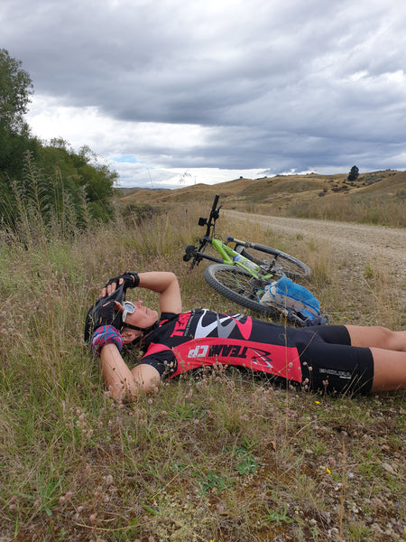 tired women laying on ground next to her bike on the side of the road