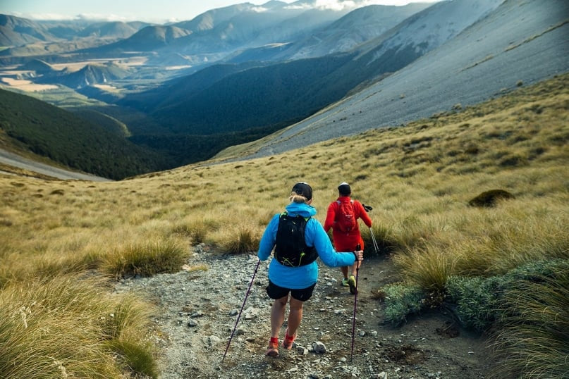 A woman and a man running down gravel in the mountains in bewteen tussocks