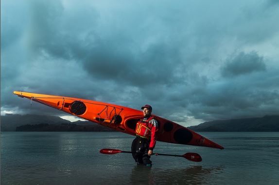 Man holding a sea kayak on his shoulder standing in the sea