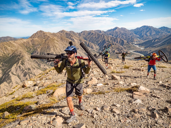 A group of people carrying mountain bikes on their shoulders up a mountain