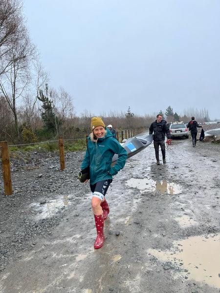 Woman wearing a rain jacket and gumboots carrying a kayak