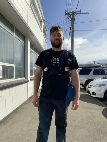 man wearing a running pack filled with snacks stands on a footpath