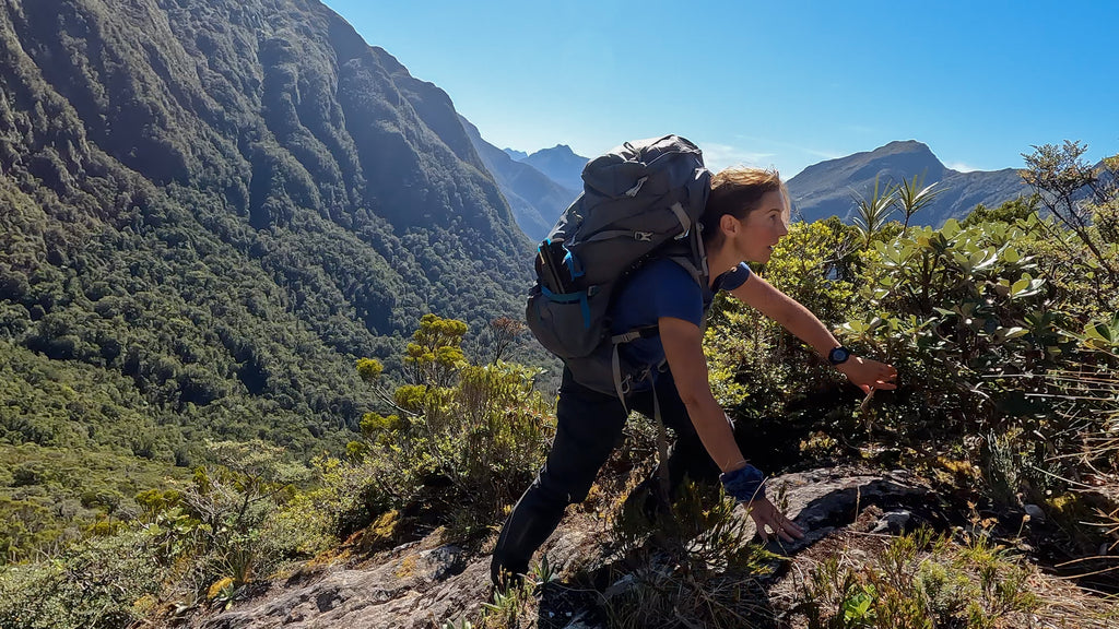 woman climbing side of mountain in bush wearing back pack