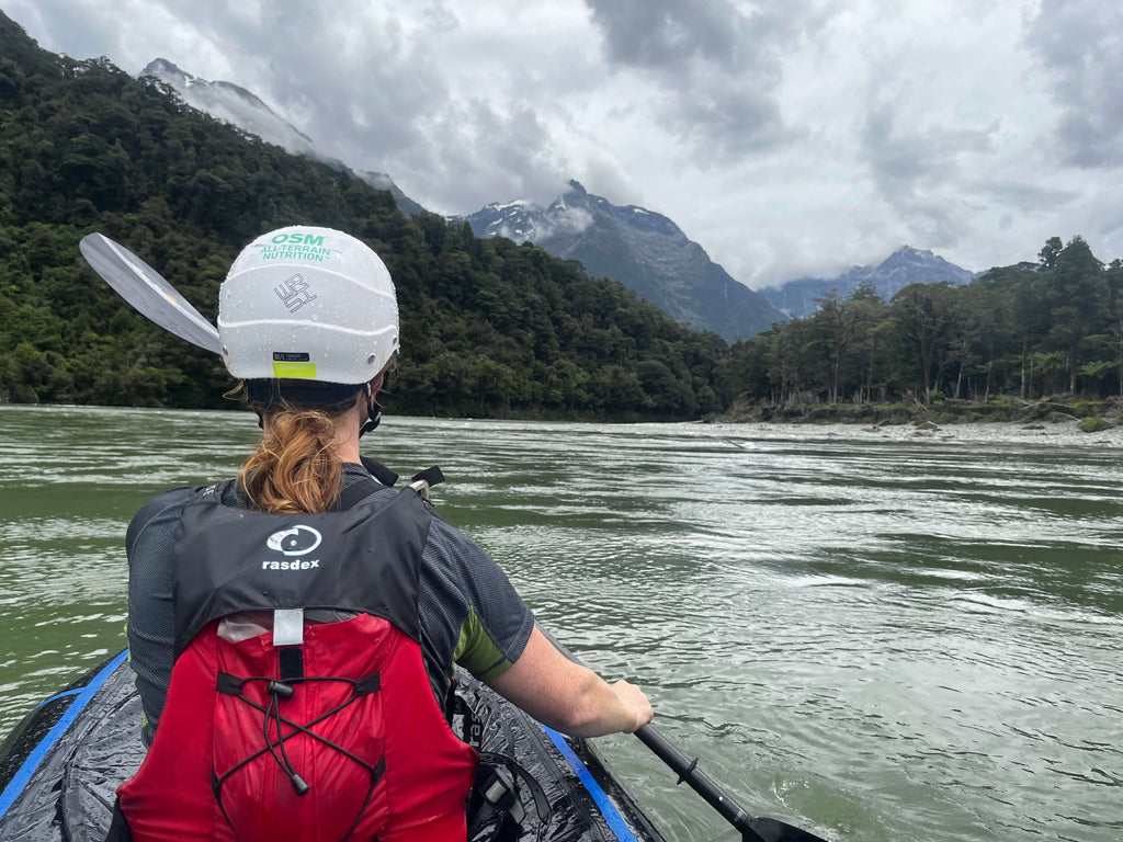 Woman in white helmet packrafting down a river mountains in the background