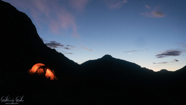 Glow of a headlamp in a tent with the silhouette of mountains in the background.