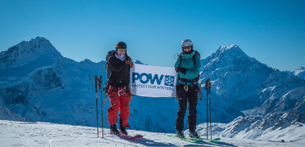 Two Skiers holding a POW "Protect Our Winters" banner in front of a backdrop of snowy mountains. 